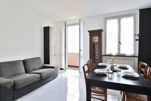 Un soggiorno moderno con un divano grigio, un tavolo da pranzo apparecchiato con piatti e tazze, e un'ampia finestra con tende.