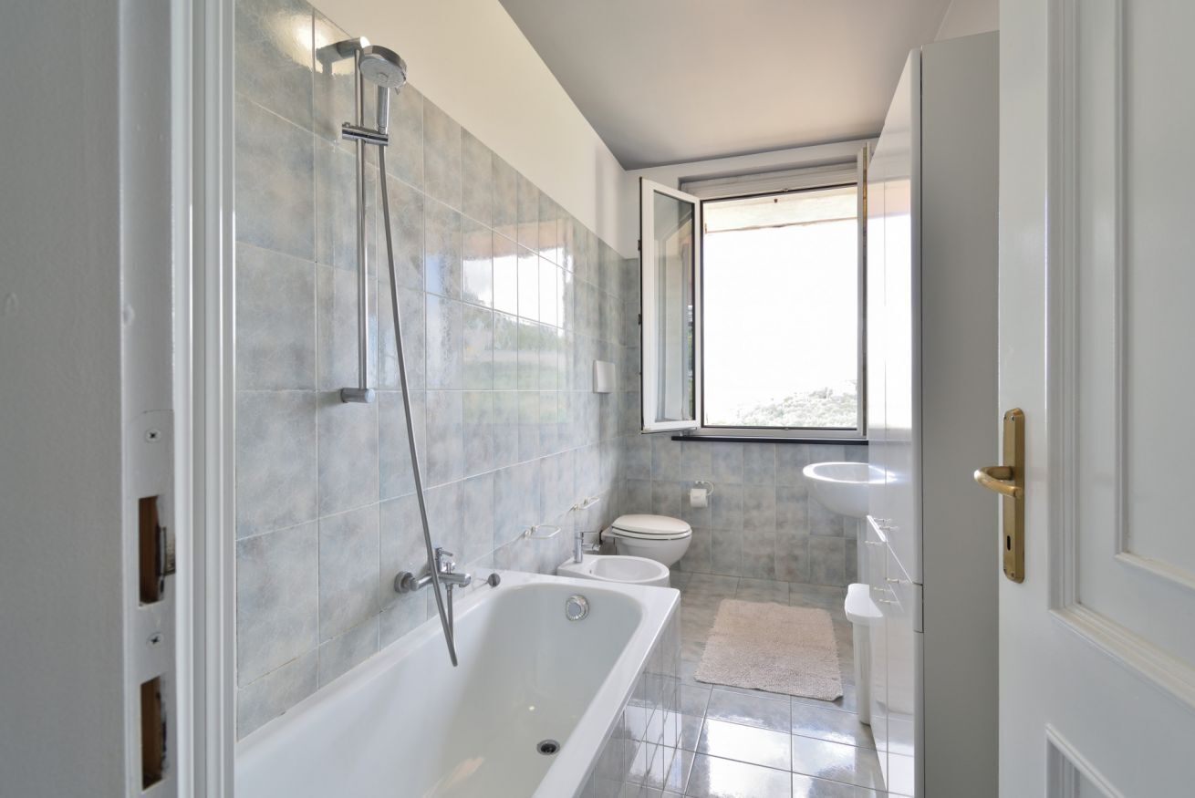 Un bagno moderno con vasca, water e lavabo, con una grande finestra e pareti in piastrelle.