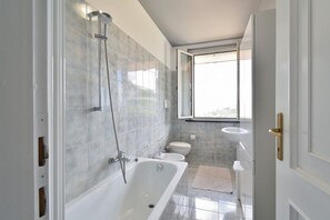 Un bagno moderno con vasca, water e lavabo, con una grande finestra e pareti in piastrelle.
