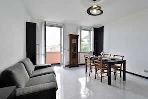 Ein modernes Wohnzimmer mit einer Couch, einem Esstisch, Stühlen, einer Uhr und einem Fenster.