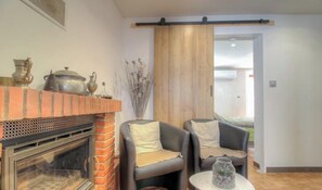 Un salon doté d’une cheminée, de deux fauteuils en cuir, d’une petite table sur laquelle est posé un vase, et d’une porte coulissante en bois.