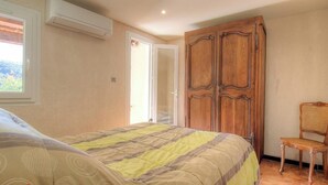 Un dormitorio con cama, aire acondicionado, armario y una silla.