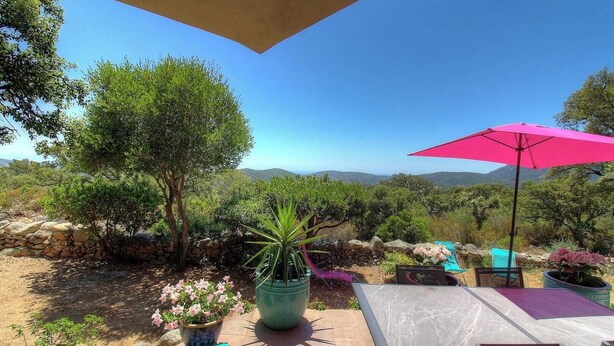Un patio con un muro in pietra, piante in vaso, un ombrellone rosa e vista sulla campagna.