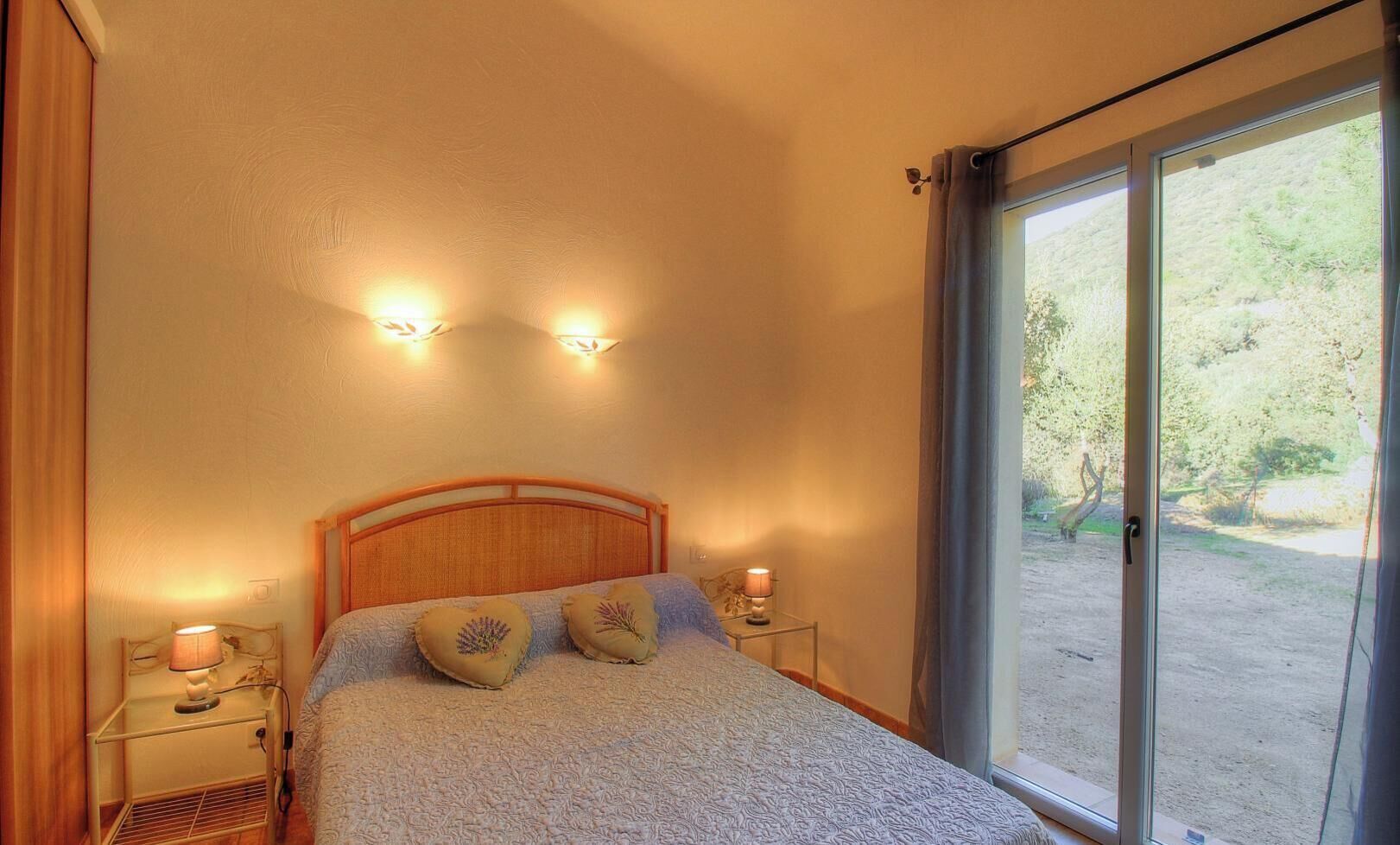 Een slaapkamer met een bed, twee bedlampen, een nachtkastje en een uitzicht door een groot raam.