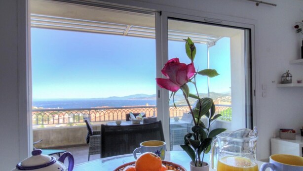 Un balcone con un tavolo apparecchiato per la colazione, un vaso con un fiore e vista sul paesaggio.