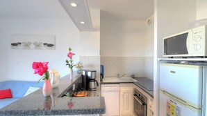 Una cucina moderna con forno integrato, microonde e frigorifero. Si può vedere una macchina del caffè, un bollitore e un lavello. Sullo sfondo, un divano blu.
