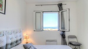 Una camera da letto con un letto, una sedia, una finestra con tende, un termosifone e una lampada.