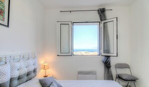 Ein Schlafzimmer mit einem Bett, einem Sessel, einem Fenster mit Vorhängen, einer Heizung und einer Lampe.