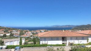 Una zona residenziale costiera con edifici a tetto di tegole rosse, un cielo azzurro limpido e vista sul mare.