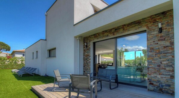 A modern house with a patio, outdoor seating, and a large sliding glass door leading to an interior space. - Villa Corsu - PORTO VECCHIO (PORTO VECCHIO)