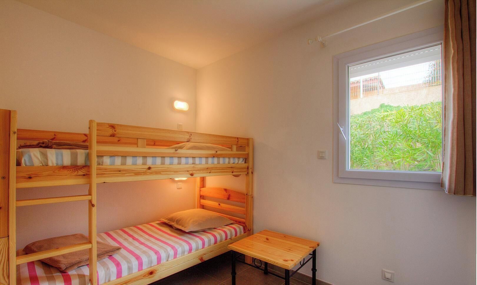 Une chambre avec un lit superposé, une petite table et une fenêtre avec des rideaux.