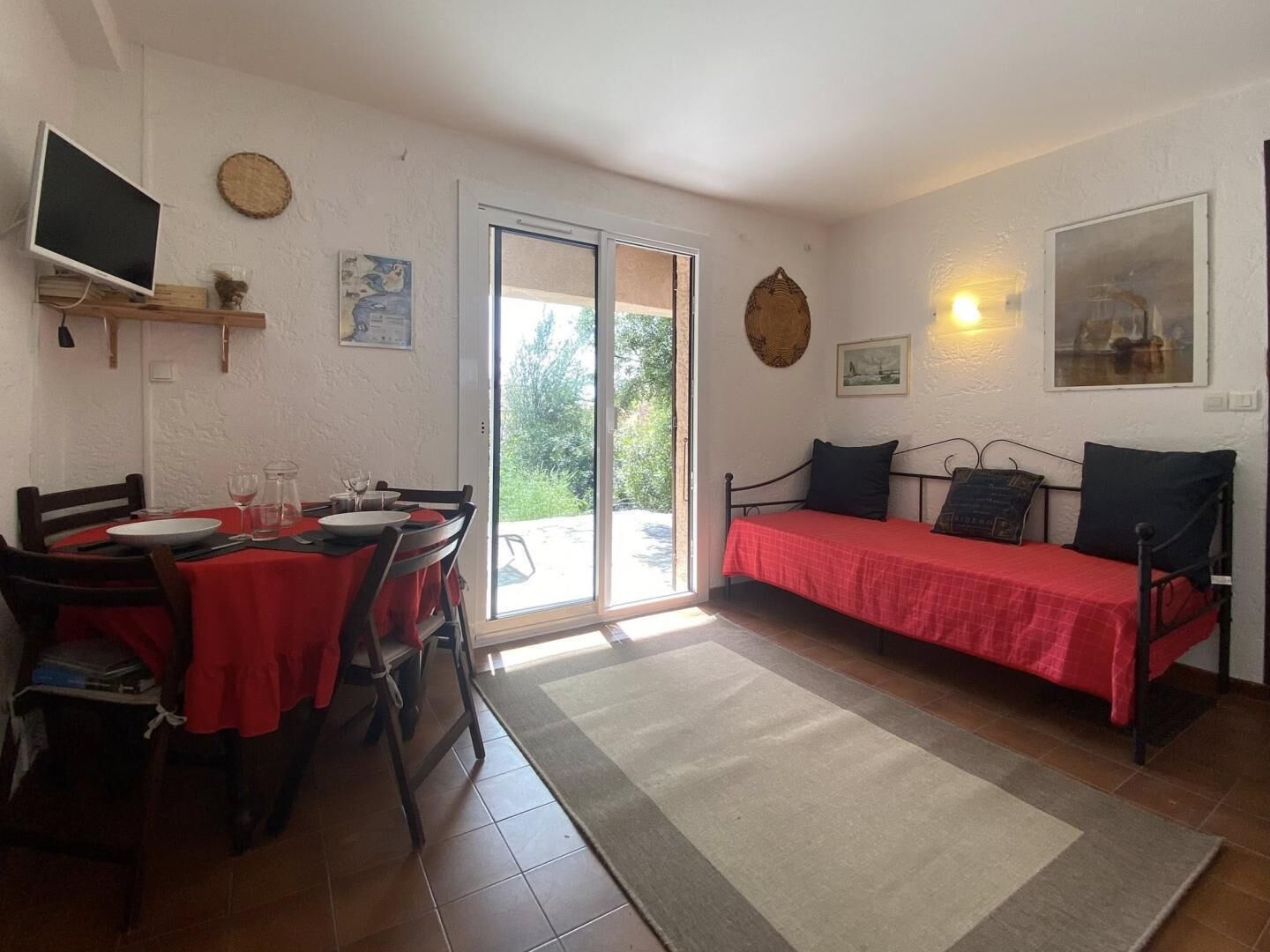 Ein Zimmer mit Esstisch, Stühlen, einem Bett und einer Glastür, die zu einem Garten führt.