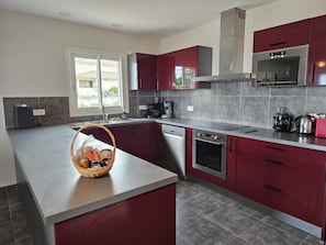 A modern kitchen with a central island, stainless steel appliances, and red cabinetry. - Santa Giulia - SOLENZARA (SOLENZARA)