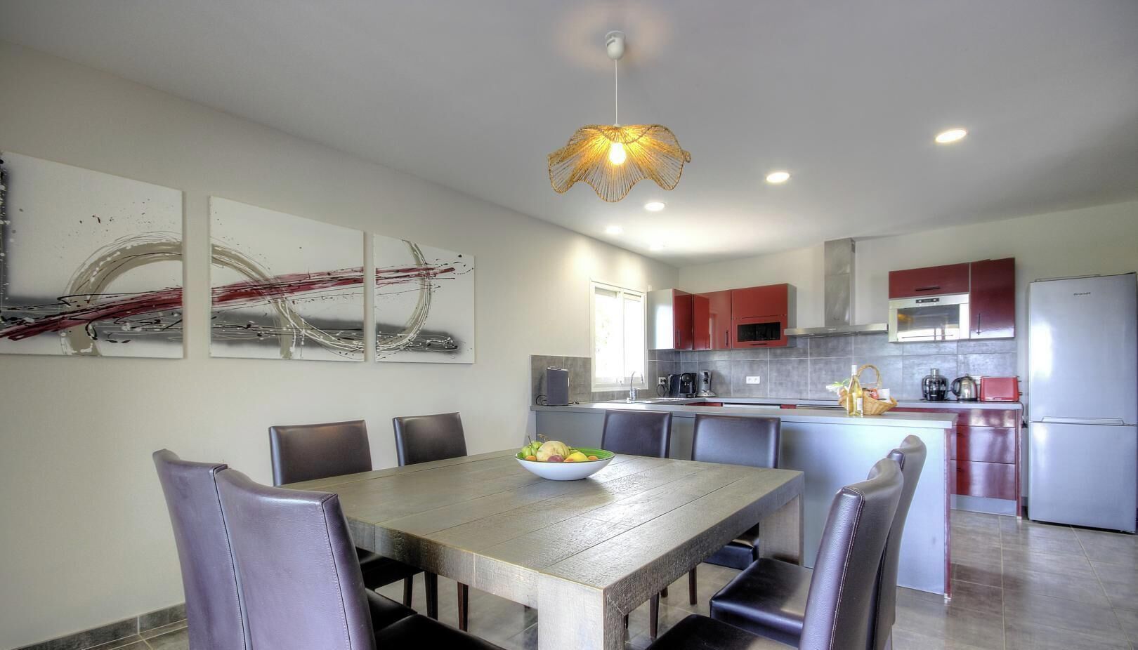 Una cocina moderna con armarios rojos, una isla central y un comedor con mesa y sillas de madera.
