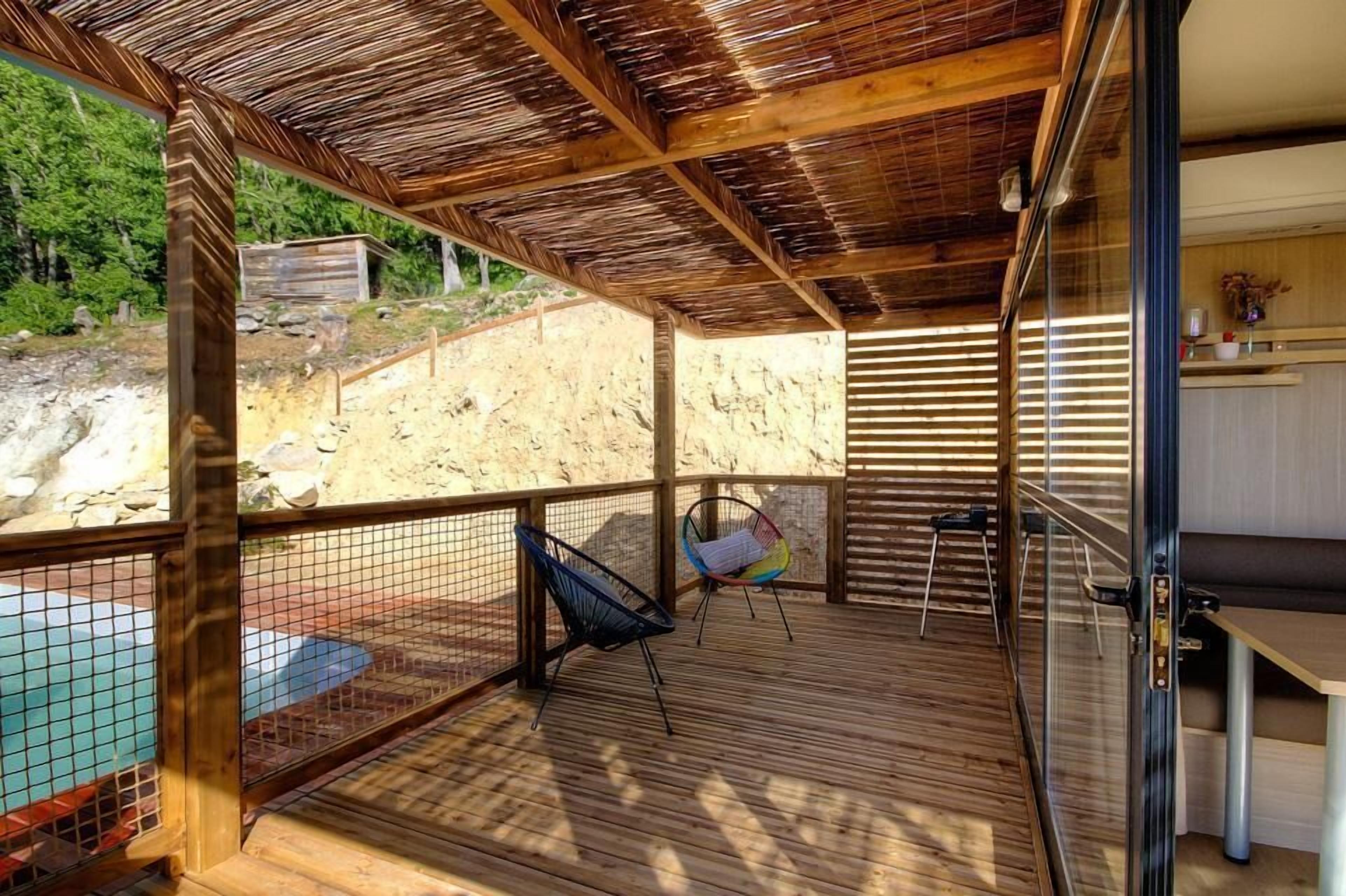 Una terraza de madera con techo de paja, una piscina y un área de descanso con sillas.