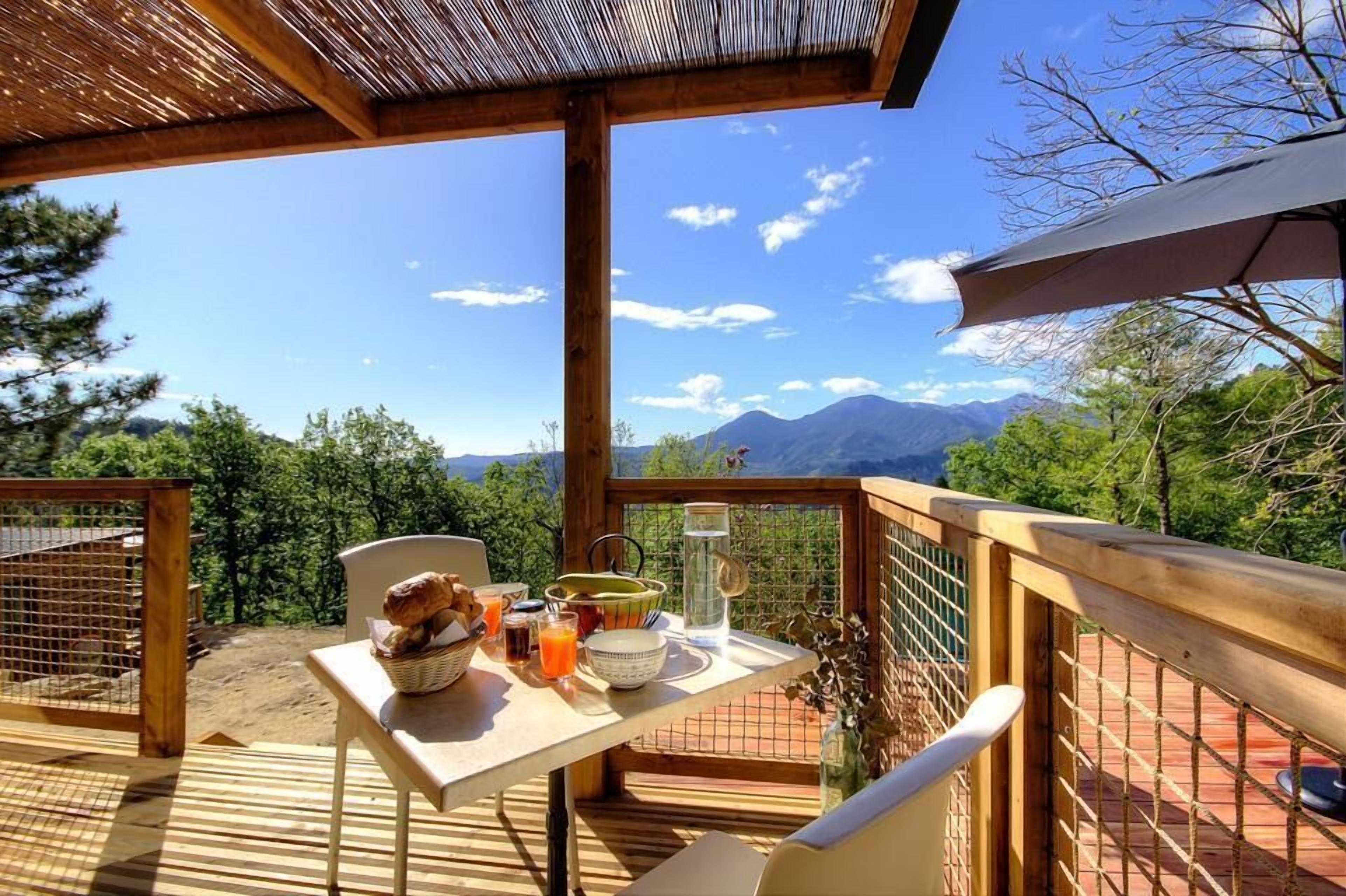 A wooden deck with a table set for breakfast, overlooking a mountainous landscape.