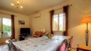 Una habitación con una mesa de comedor, sillas, un televisor, una lámpara y una ventana con cortinas.