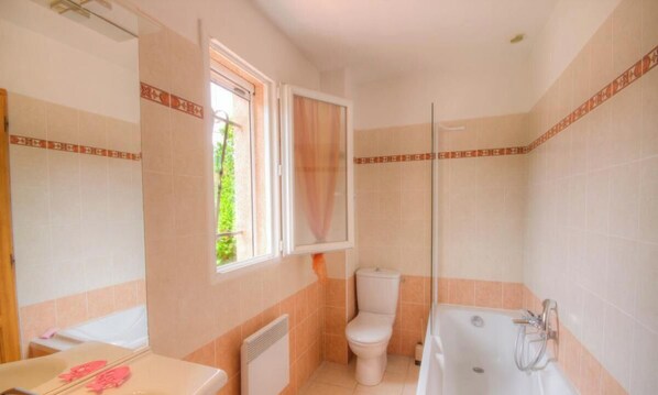 Un baño con inodoro, bañera y ventana con cortina.