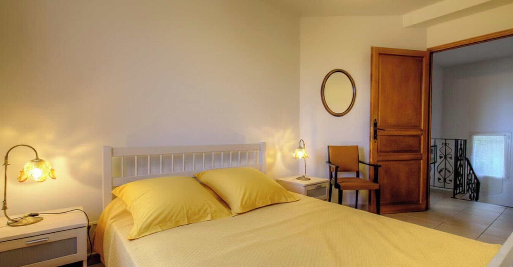 Une chambre à coucher avec un lit, des lampes de chevet, une chaise, une armoire en bois et un miroir au mur.