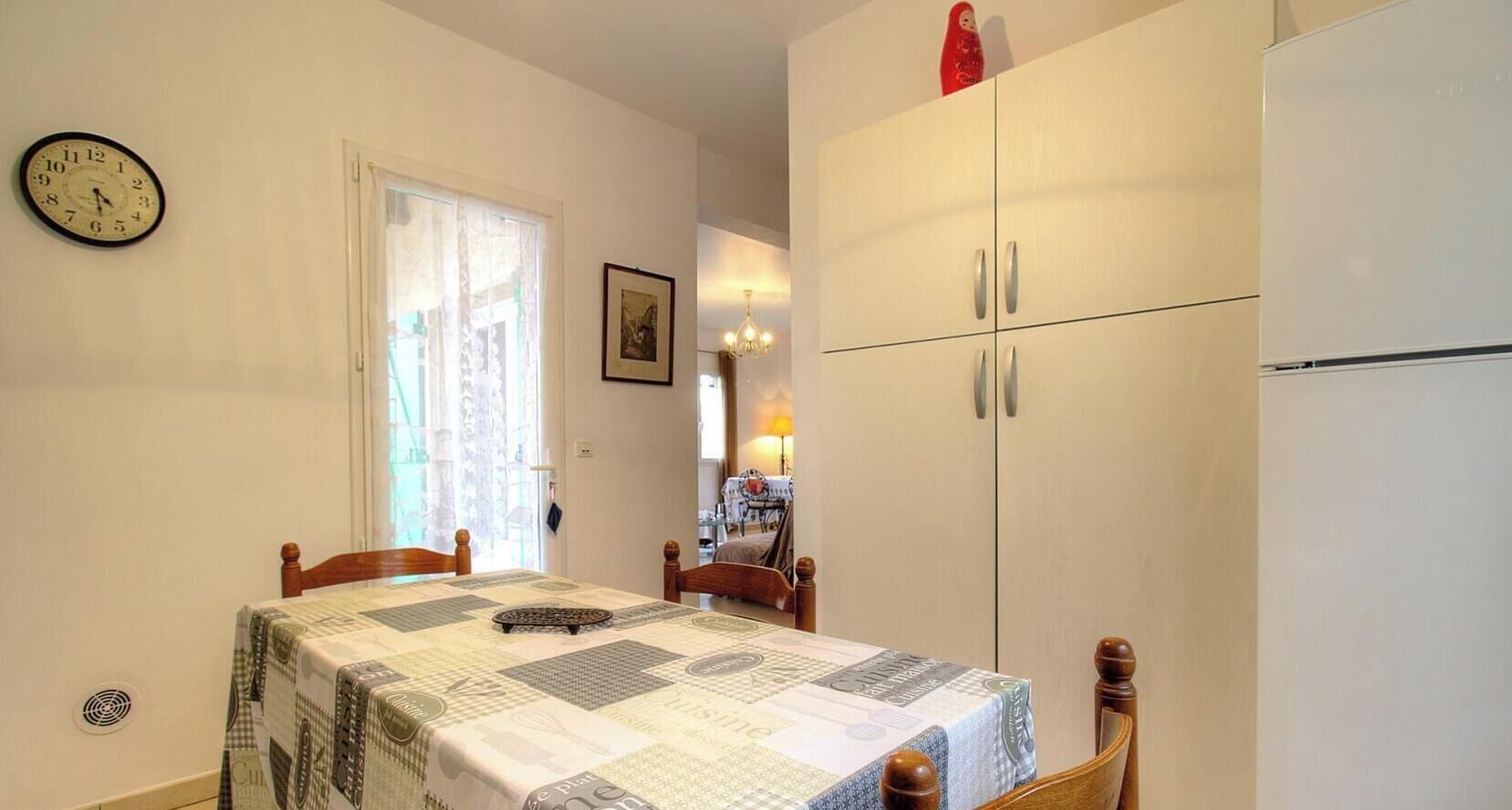 A dining area with a table set for two, a clock on the wall, and a cabinet with two doors.