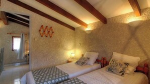 Une chambre avec deux lits, des poutres en bois, un mur en pierre, une petite fenêtre et une table de chevet avec une lampe.