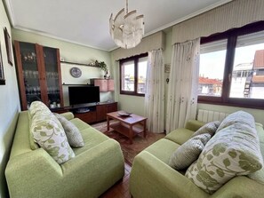 Un salon avec deux canapés verts, une table basse en bois, un téléviseur et une fenêtre avec des rideaux.