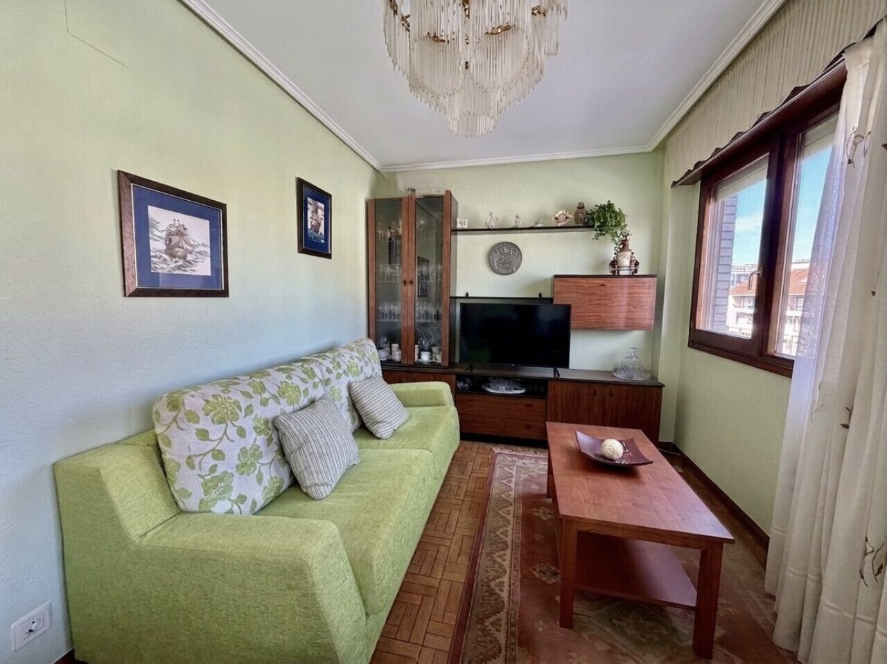 A living room with a green sofa, a wooden coffee table, a television, and a cabinet.