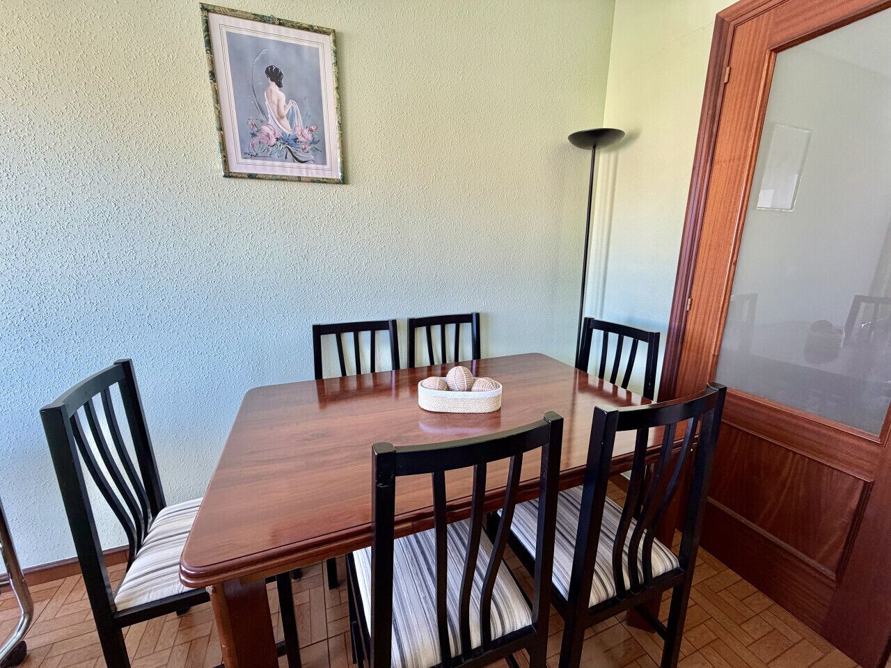 Uma mesa de jantar com cadeiras, um quadro na parede e uma porta com vidro fosco.