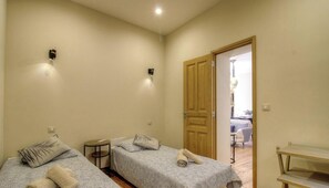 Ein Zimmer mit zwei Betten, einem kleinen Tisch und einer Tür zu einem anderen Raum.