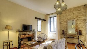 A living room with a fireplace, a television, a dining table, and a stone wall. - Casa Citadella - BONIFACIO (BONIFACIO)