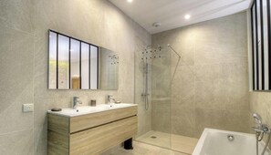 Ein modernes Badezimmer mit einem großen Spiegel, zwei Waschbecken, einer Dusche und einer Badewanne.