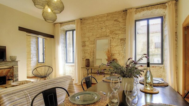 A dining area with a stone wall, a fireplace, and a table set for two with wine glasses and a vase of flowers. - Casa Citadella - BONIFACIO (BONIFACIO)