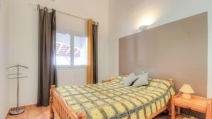 Un dormitorio con cama, mesita de noche, lámpara, ventana con cortinas y una lámpara de pie.