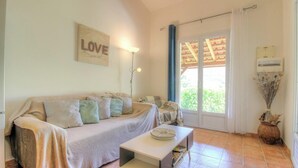 Una sala de estar acogedora con sofá, una mesita de centro, una lámpara y un amplio ventanal con cortinas.