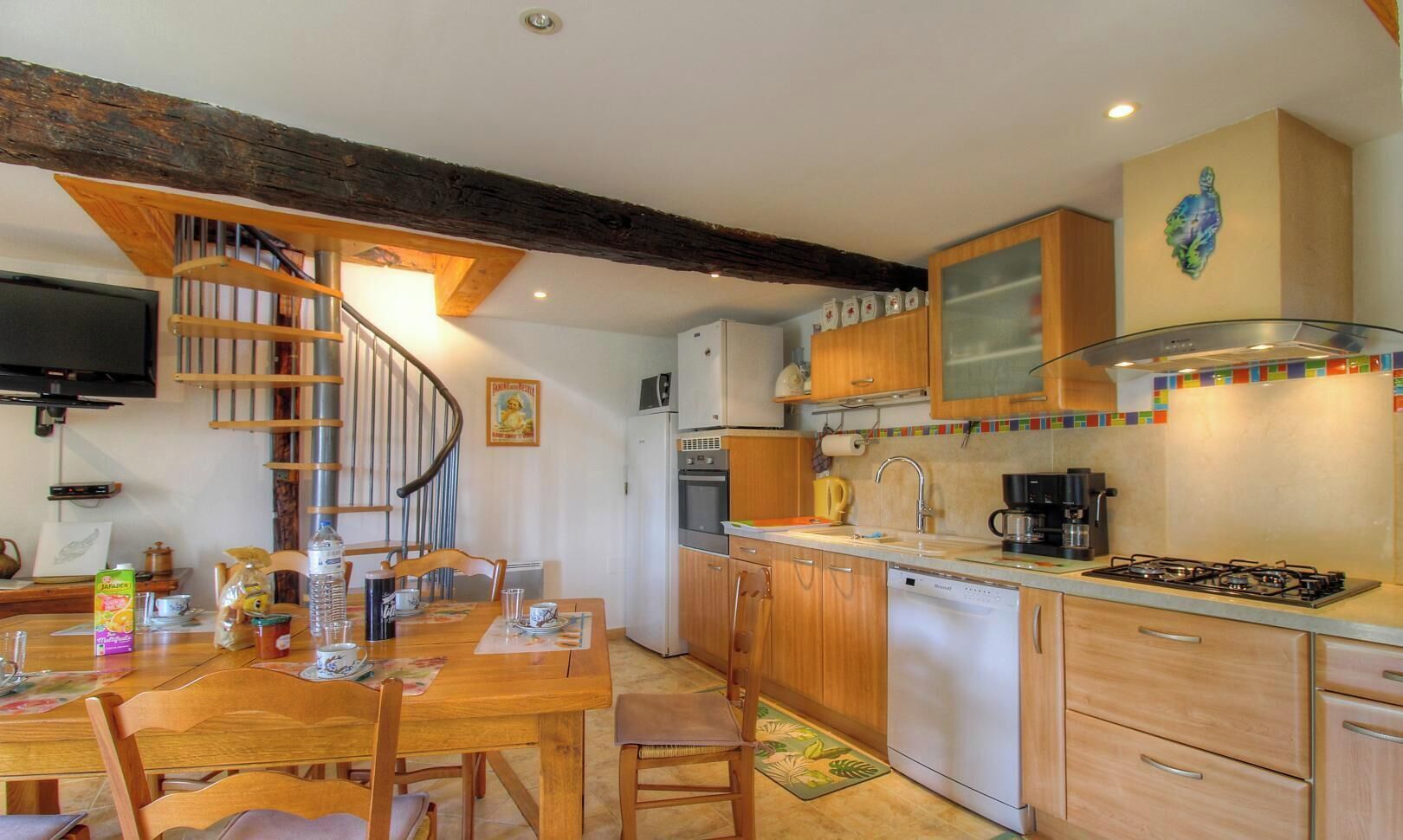 Une cuisine avec des meubles de rangement en bois, une cuisinière encastrée et un coin repas comprenant une table et des chaises en bois.
