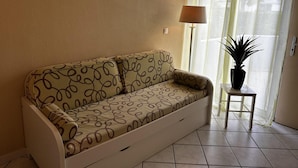 Uma sala de estar com um sofá, uma mesinha com uma planta e três quadros na parede.