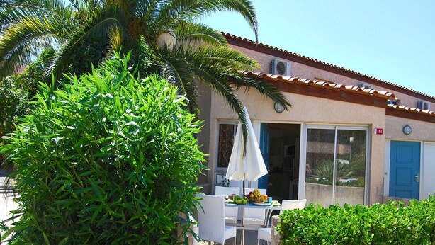 Um edifício com telhado de azulejos, uma porta com número e mesas com cadeiras na parte externa.