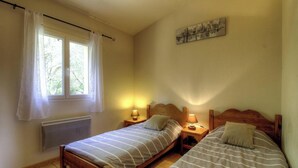 A bedroom with two beds, a radiator, a window with curtains, and a wall-mounted artwork. - Ogliastrello sheepfolds (FIGARI)