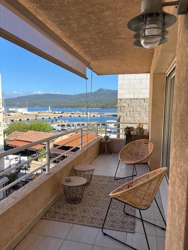 Ein Balkon mit Blick auf eine Marina, Korbstühle, ein kleiner Tisch und ein gemustertes Teppich.