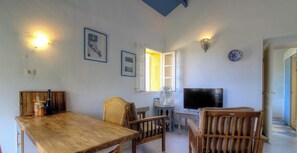 Ein Wohnzimmer mit Holztisch, Korbstühle, Fernseher und Wandleuchten.