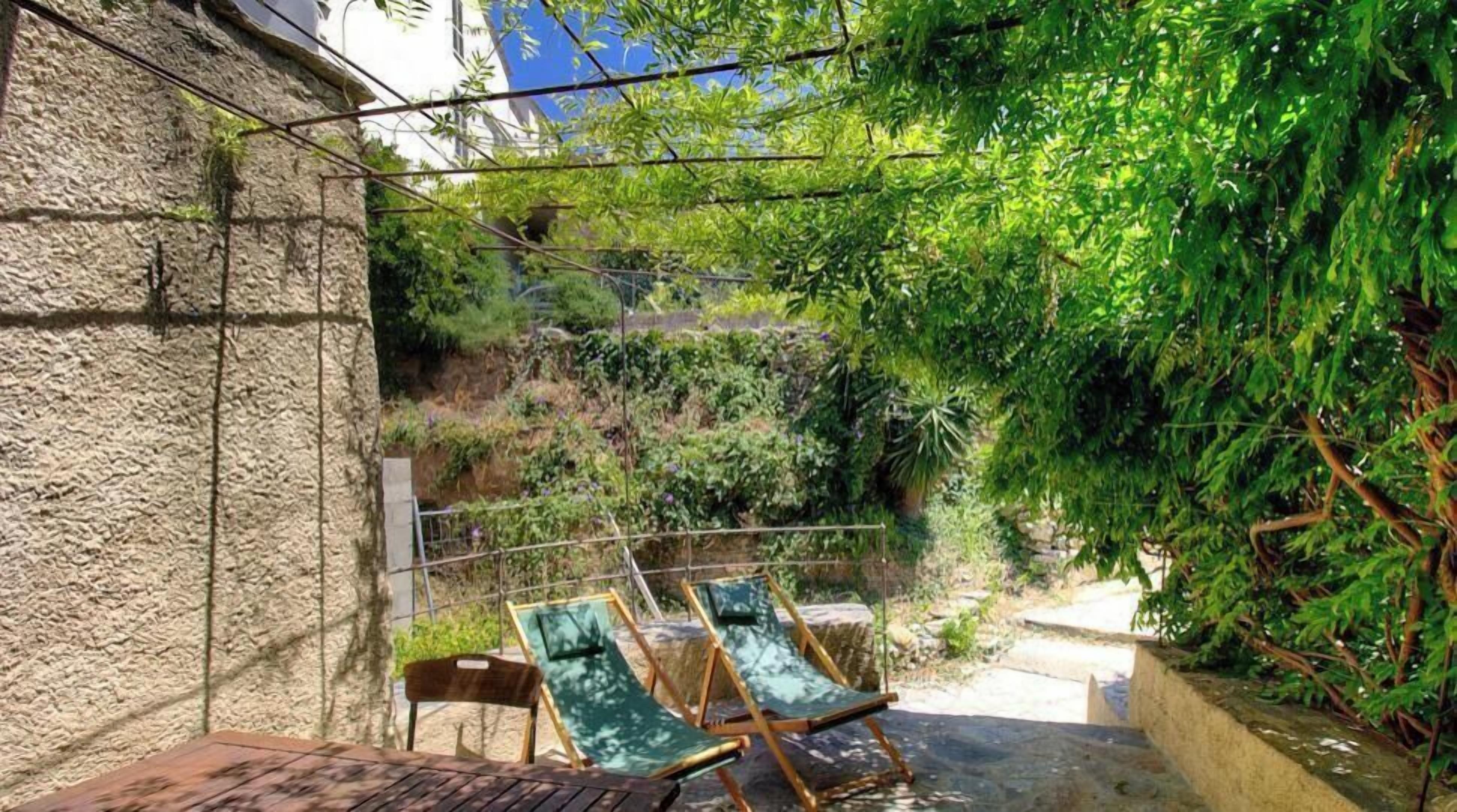 Une terrasse avec deux chaises longues, un mur en pierre et un feuillage dense.