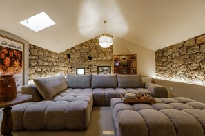 Ein gemütliches Wohnzimmer mit Steinwand, einem Ecksofa, einem Holztisch und einem Bücherregal.