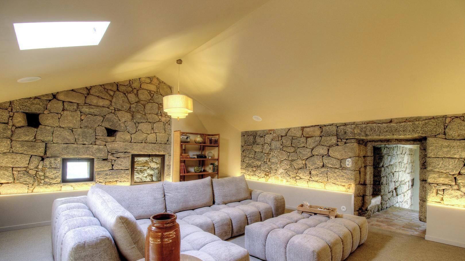 A modern living room with a stone wall, a sectional sofa, a wooden bookshelf, and a fireplace.