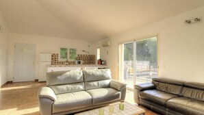 A spacious living room with two leather sofas, a kitchen area, and a sliding glass door leading to an outdoor patio. - Villa chjara - SAINTE LUCIE DE PORTO VECCHIO (SAINTE LUCIE DE PORTO VECCHIO)