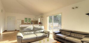 Ein geräumiges Wohnzimmer mit zwei Ledersofas, einer Küchenzeile und einer Glasschiebetür, die auf eine Terrasse im Freien führt.
