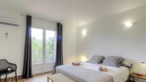 A bedroom with a bed, a chair, a bedside table, and a window with curtains. - Villa chjara - SAINTE LUCIE DE PORTO VECCHIO (SAINTE LUCIE DE PORTO VECCHIO)