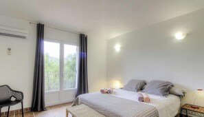 Ein Schlafzimmer mit Bett, Stuhl, Nachttisch und einem Fenster mit Vorhängen.