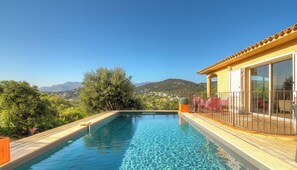 Ein Schwimmbad mit Holzterrasse, überdachter Veranda und Blick auf ferne Hügel.