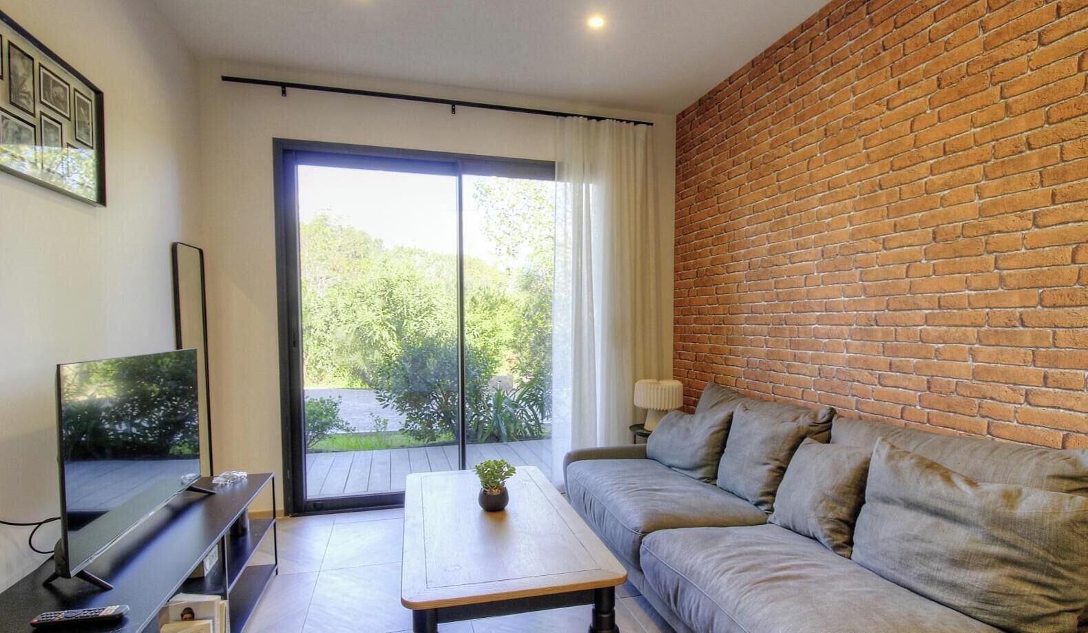 A modern living room with a sofa, a coffee table, a TV, and a brick wall.