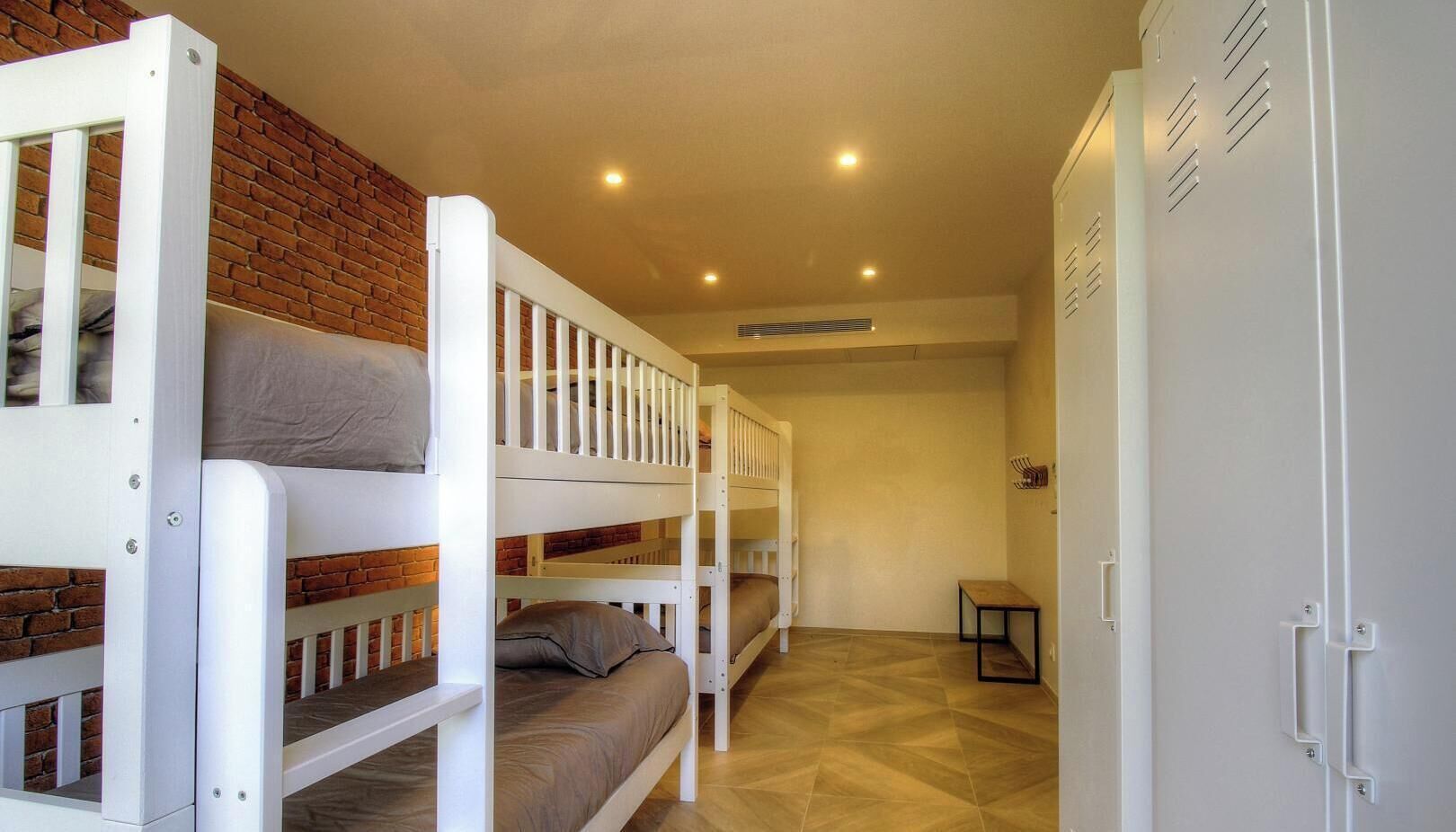 A bunk bed room with a brick wall, a small table, and a wardrobe.